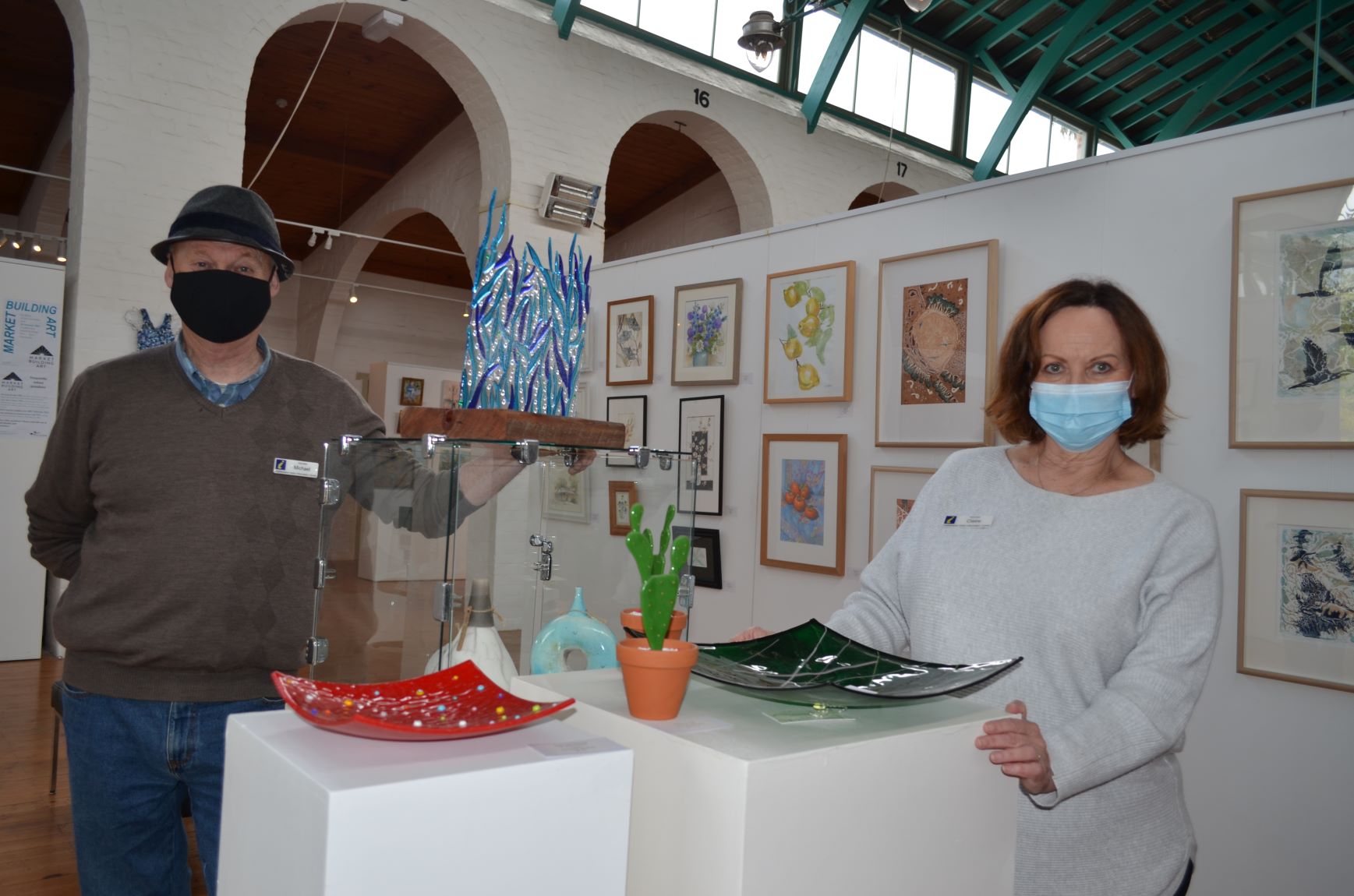 Castlemaine Visitor Centre volunteers Michael and Claire are pictured with some of the beautiful artworks on display at the Historic Market Building.