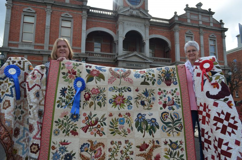 Elli Henry and Pattie Ritchie are pictured with their award winning quilts and the raffle quilt (centre).